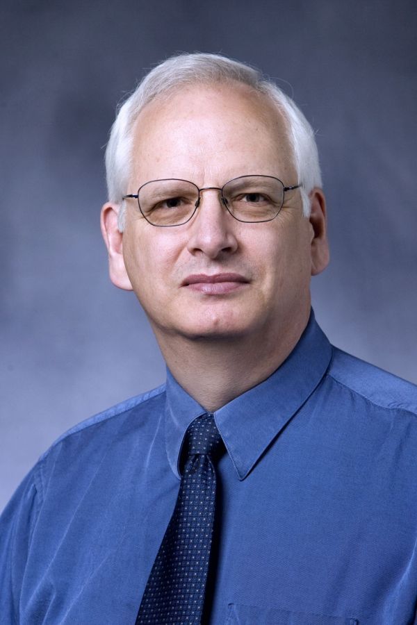 Randy Maddox headshot in blue shirt, blue tie, and black rimmed glasses