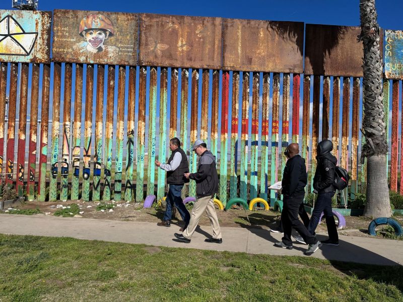 Faculty walk past the U.S.-Mexico border which is painted with a colorful mural
