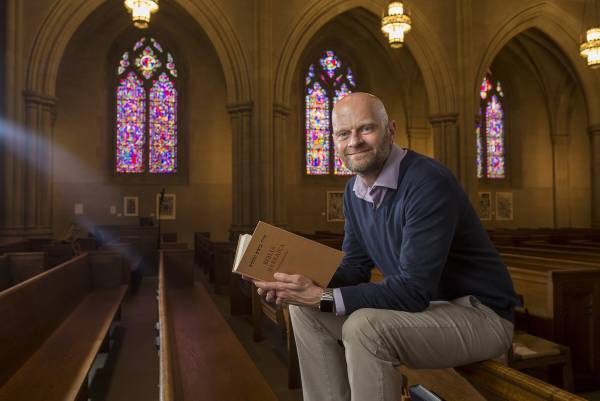 Brent Strawn sits in a pew in Duke Chapel holding a Hebrew Bible.