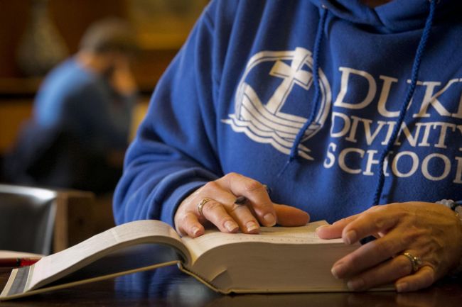 A student reads a book while wearing a Duke Divinity logo sweatshirt