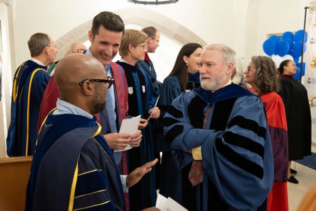 Faculty members chat in the hallway wearing regalia before Closing Convocation
