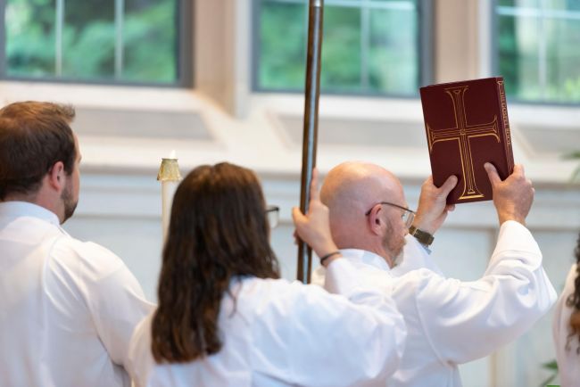 A student in white robes holds a bible aloft in Goodson Chapel
