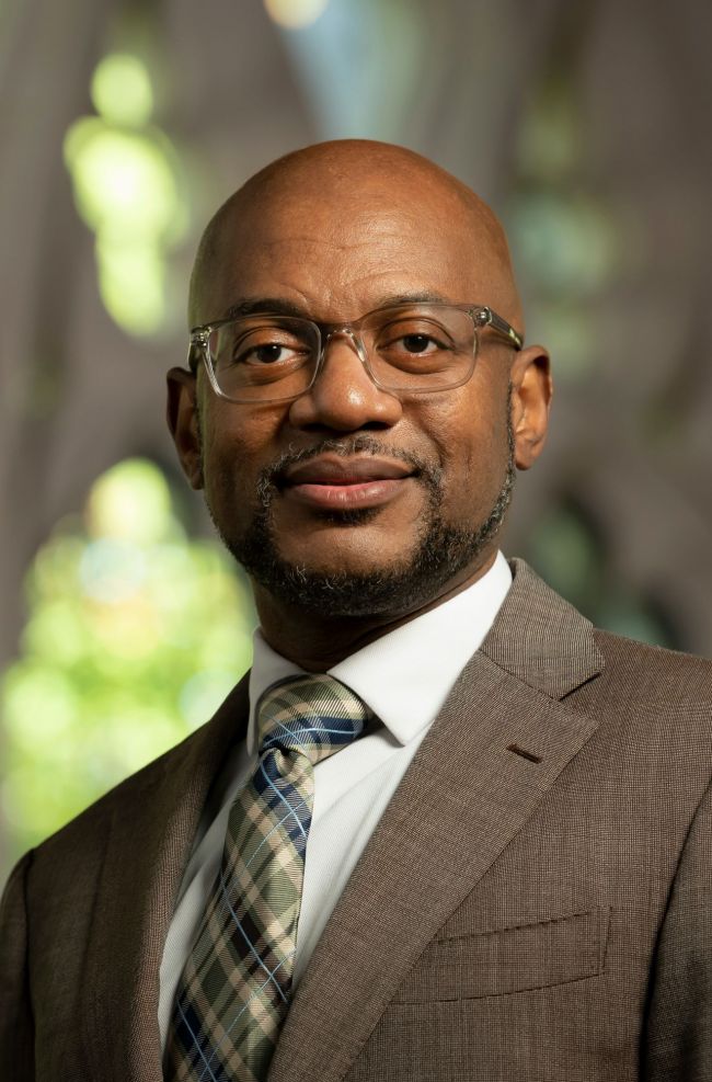 Norbert Wilson headshot, he wears a brown suit and plaid tie