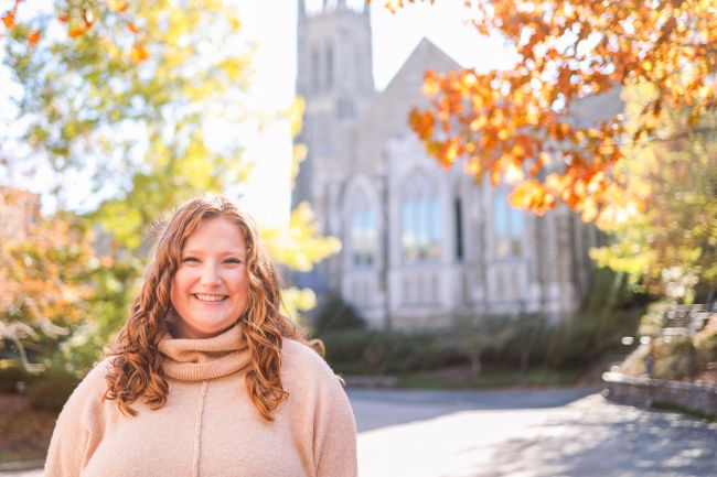 Baptist student  in tan sweater outside Goodson chapel; trees with fall-colored leaves surrounding
