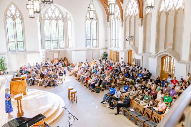 Students gathered in a full Goodson Chapel for orientation with a woman in a blue dress speaking from the putpit