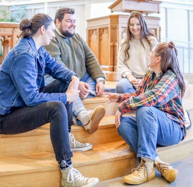 Methodist Students sit on stairs of altar in Goodson while smiling and laughing