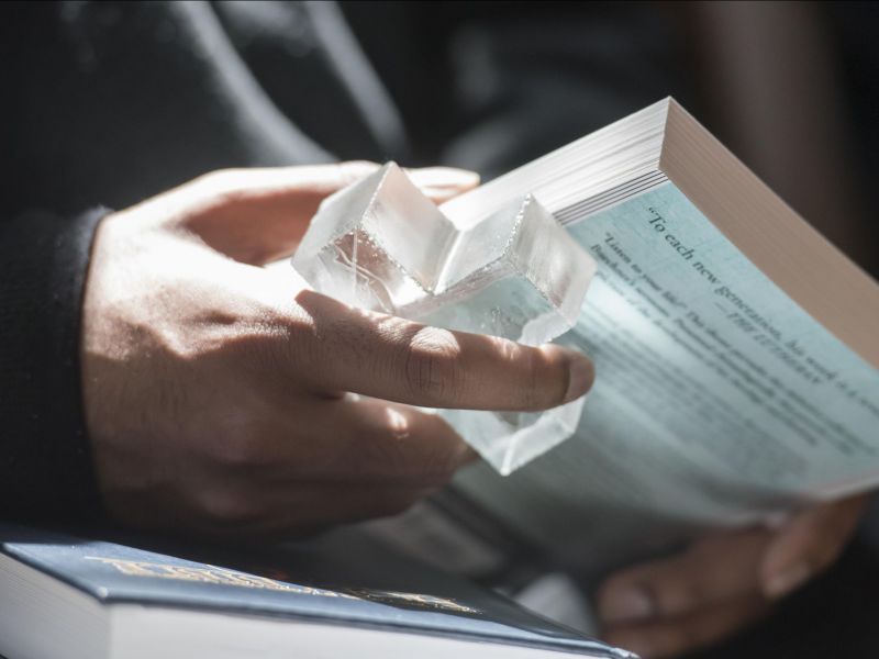 Hands hold a clear glass cross and a book