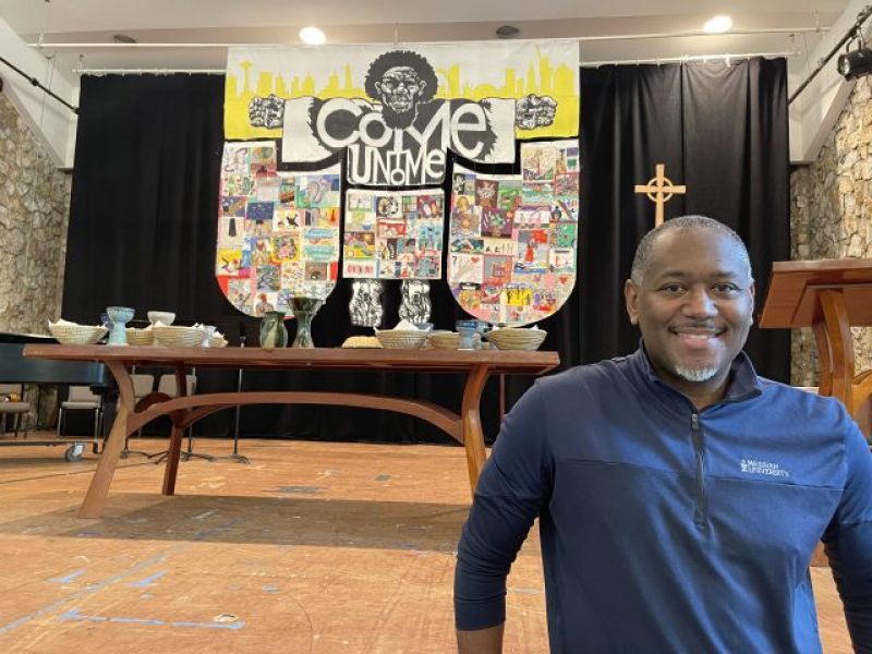 Man standing in front of quilt behind a communion table