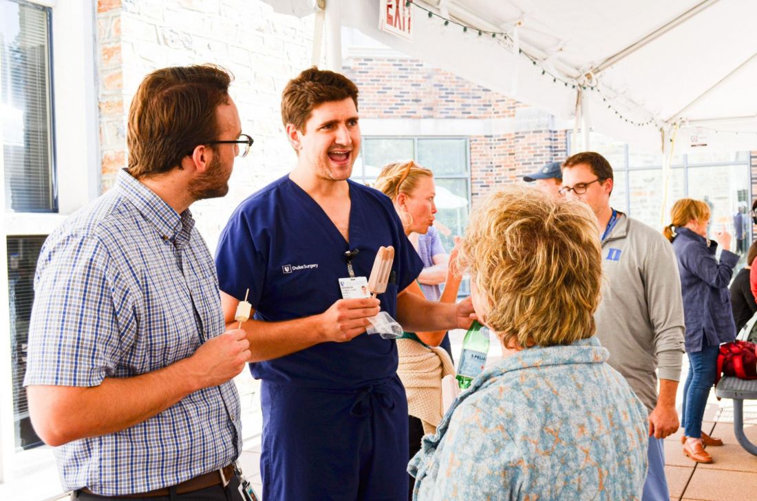 A man wears Duke Surgery scrubs while talking to other people on a patio