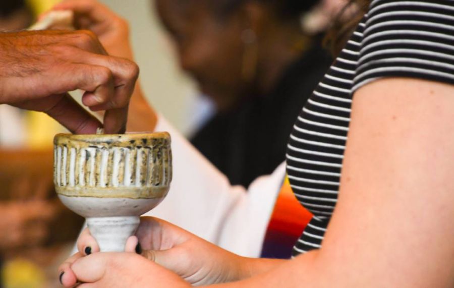 Hand dips communion bread into a ceramic communion cup.