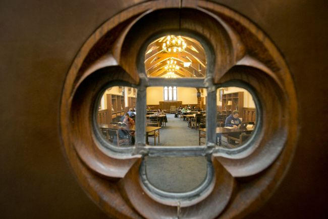 Students are visible studying through a clover-shaped window in a wooden door