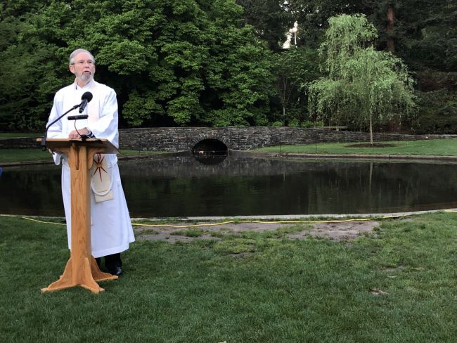 Richard Hays preaching in white clerical robes in front of pond at Duke Gardens