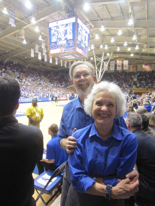 Richard and Judy Hays embrace while wearing blue shirts inside the arena watching a Duke basketball game