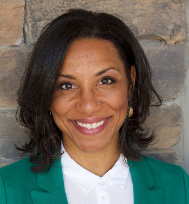 Woman in green blazer and white shirt smiles, looking at the camera