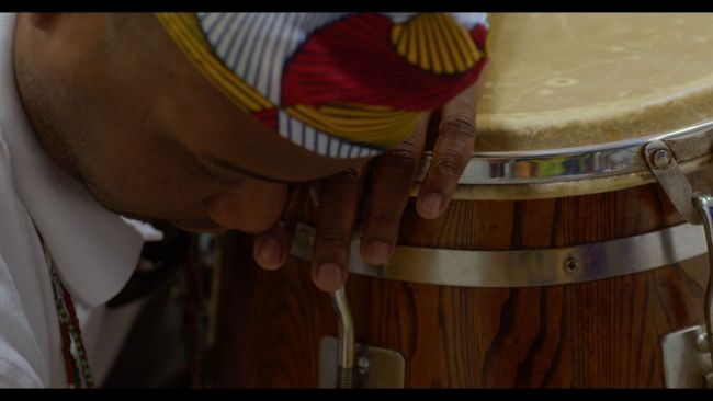 A man wearing a african print hat leans on a conga