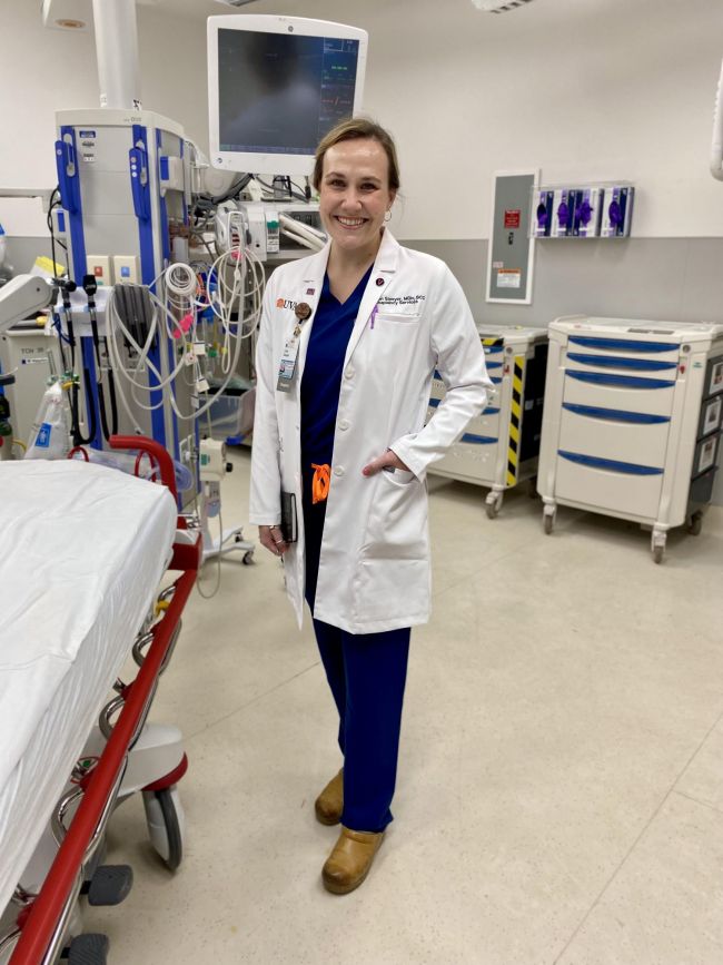 Alumnus Rev. Carly Sawyer wearing a white coat standing in the Trauma Bay in the ED at the UVA Medical Center
