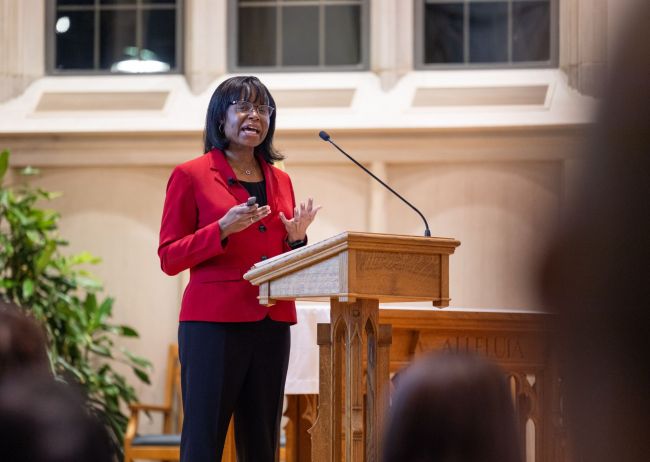 Dr. Kimberly Johnson, wearing a red blazer, speaks at the podium in Goodson Chapel