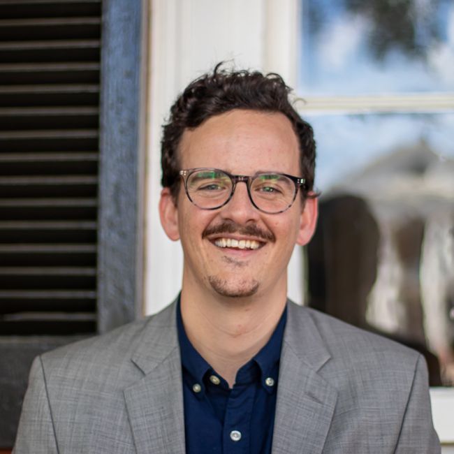 Caucasian male with glasses, blue shirt and neutral color blazer