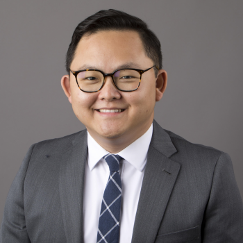 Andrew Kim wearing glasses, a grey blazer and a navy tie