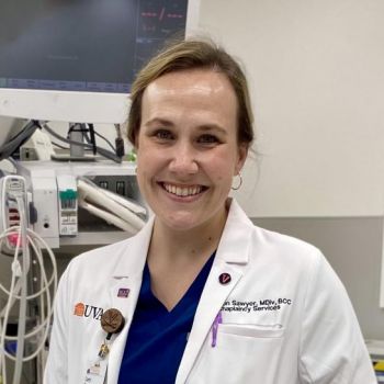 Alumnus Rev. Carly Sawyer wearing a white coat standing in the Trauma Bay in the ED at the UVA Medical Center