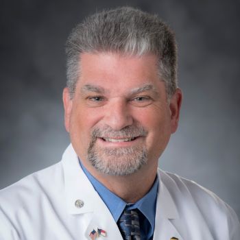 Michael Haglund smiling wearing a blue shirt and tie under a white medical coat