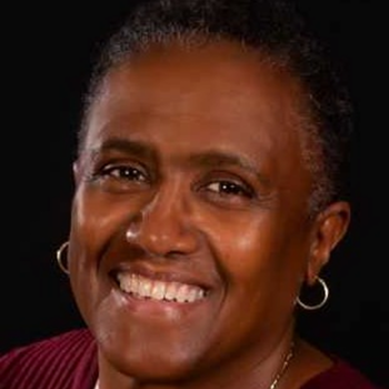 Kim Ramsey-White smiling wearing a red sweater and gold cross necklaces