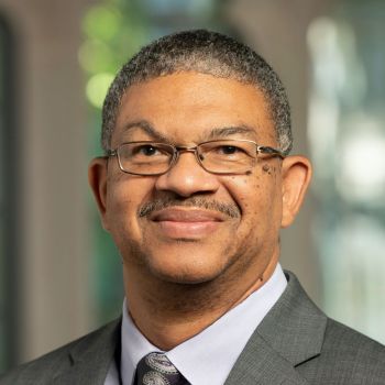 Michael Long headshot in front of Goodson Chapel windows, in dark gray suit and paisley purple tie