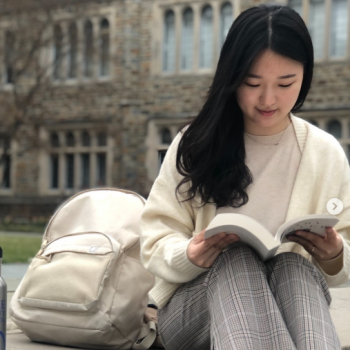 Lois Yoo reading a book on the quad