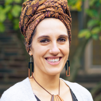 Victoria wears a head wrap and wooden jewelry with a black blouse and light grey cardigan