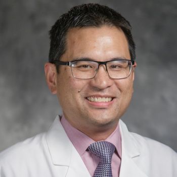 Walter Lee wearing glasses, a pink shirt and tie, with a white medical coat