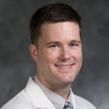 Andrew Miller wearing a shirt and tie with white medical coat