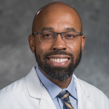 Joseph Jackson wearing glasses, a blue shirt and tie, and a white medical coat