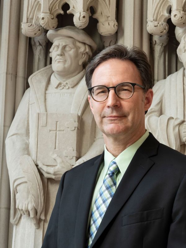 Ronald K. Rittgers headshot in front of Duke Chapel in black suit, green shirt, and blue and green tie