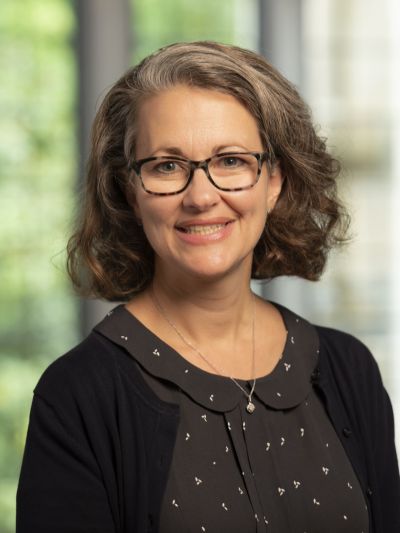 Laceye Warner headshot; she wears a demure blouse and cardigan and glasses